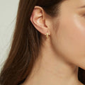 Model wearing Fleur De Lis CZ Small Huggie Earrings in Sterling Silver 0.5 inch, Yellow Gold Flashed